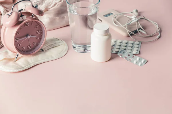 Sveglia, maschera per gli occhi, pillole e bicchiere d'acqua su sfondo rosa — Foto Stock