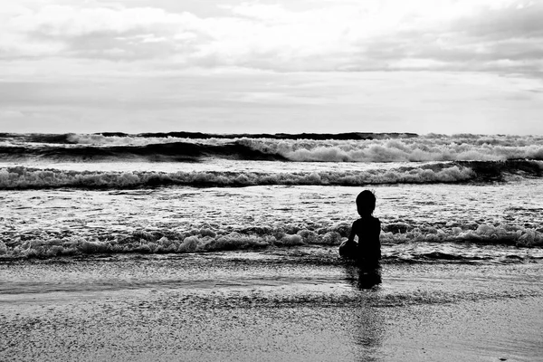 Silueta de niño que se sienta en la playa al atardecer . — Foto de Stock