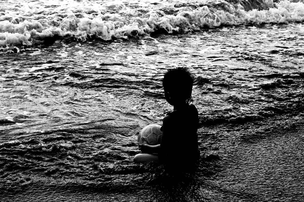 Silueta de niño que se sienta en la playa al atardecer . — Foto de Stock