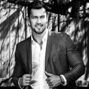 Klasik gri takım elbise teşkil ahşap çit yakınındaki zarif yakışıklı adam.