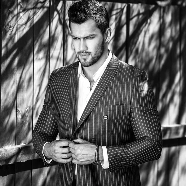 Elegante bell'uomo in classico abito grigio posa vicino alla recinzione in legno . — Foto Stock