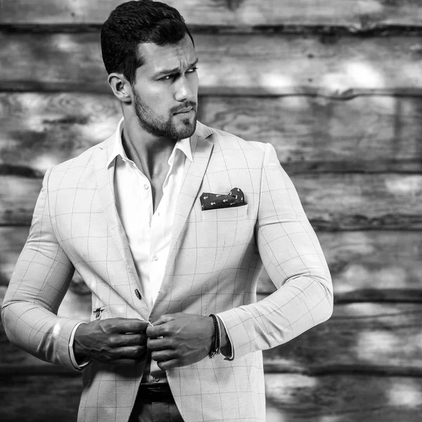 Black-white portrait of young handsome fashionable man in white suit against wooden wall