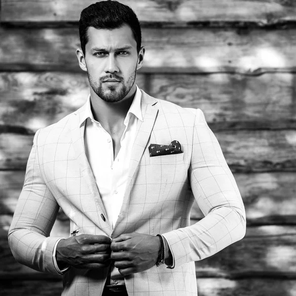 Retrato blanco y negro del joven guapo hombre de moda en traje blanco contra pared de madera —  Fotos de Stock