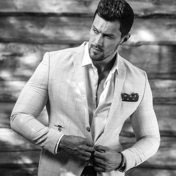 Retrato blanco y negro del joven guapo hombre de moda en traje blanco contra pared de madera —  Fotos de Stock