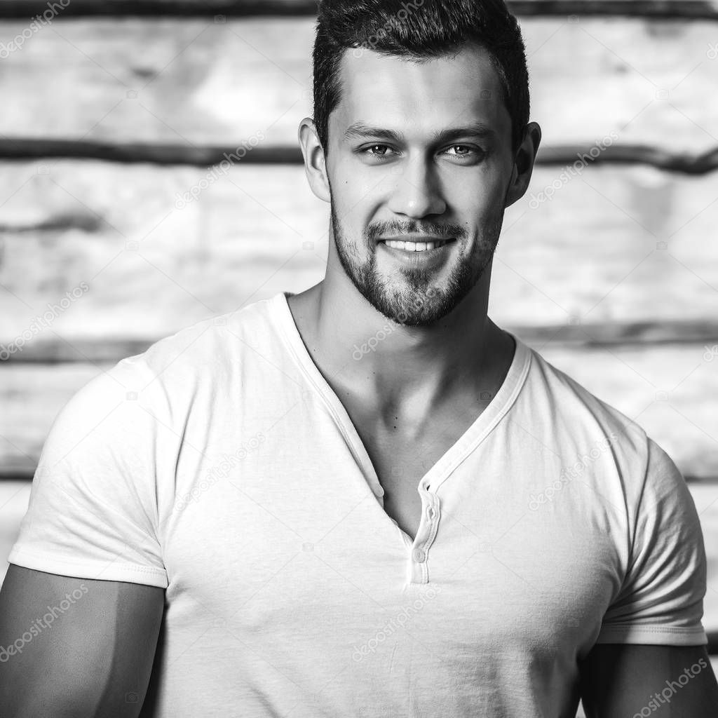 Black-white portrait of young beautiful sporty man in white t-shirt against wooden wall.