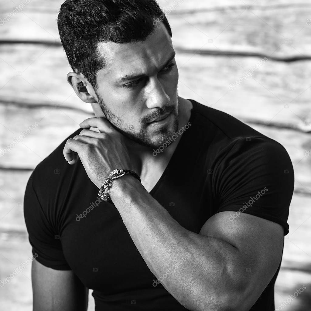 Black-white portrait of young beautiful sporty man in black t-shirt against wooden wall.