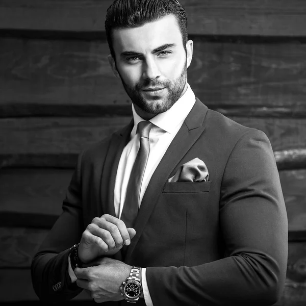 Schwarz-weißes Porträt eines schönen modischen Mannes im eleganten Anzug vor Holzhintergrund. — Stockfoto