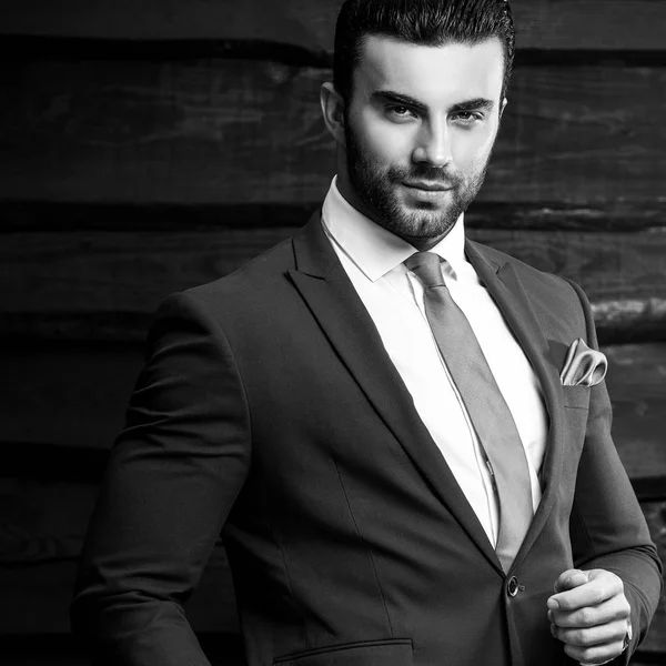 Black-white portrait of beautiful fashionable man in stylish suit against wooden background. — Stock Photo, Image