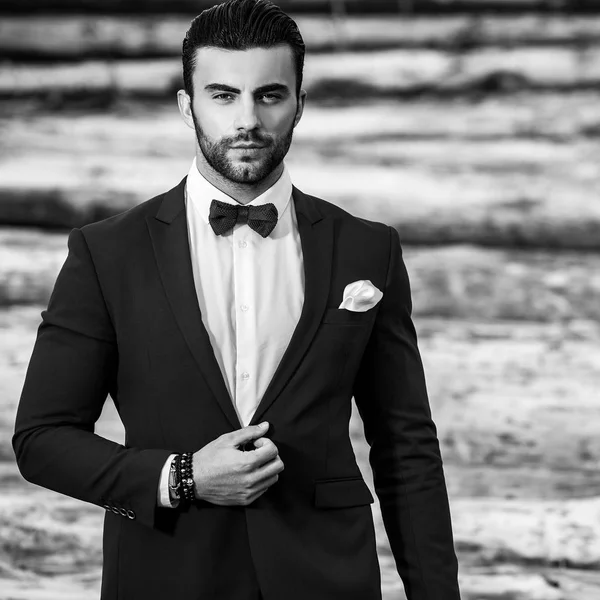 Schwarz-weißes Porträt eines schönen modischen Mannes im eleganten Anzug vor Holzhintergrund. — Stockfoto