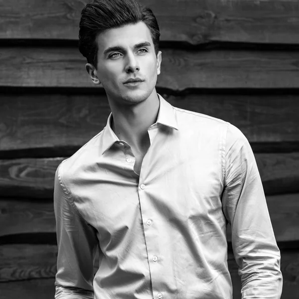 Schwarz-weißes Porträt eines jungen, gut aussehenden, modischen Mannes gegen eine Holzwand. — Stockfoto