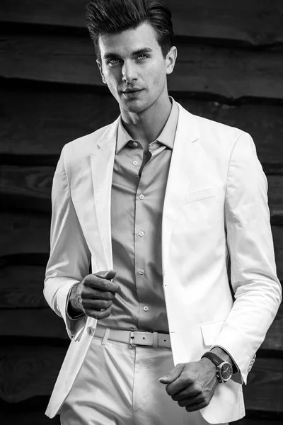 Svart-hvitt portrett av en ung, kjekk mann i hvit dress mot trevegg – stockfoto
