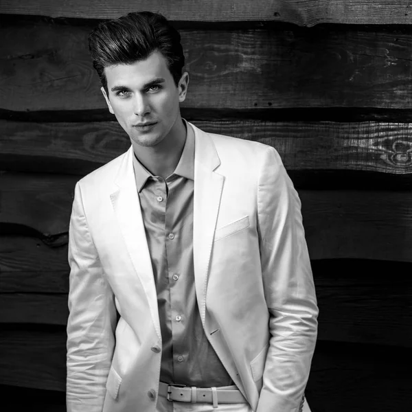 Retrato blanco y negro del joven guapo hombre de moda en traje blanco contra pared de madera —  Fotos de Stock