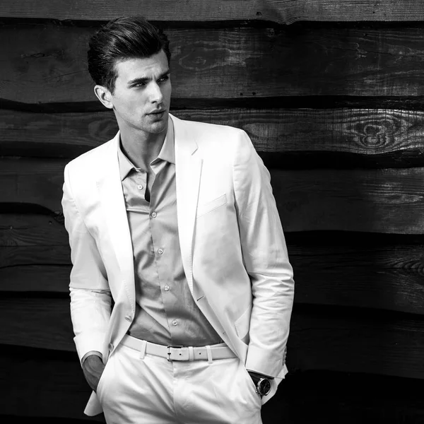 Retrato blanco y negro del joven guapo hombre de moda en traje blanco contra pared de madera —  Fotos de Stock