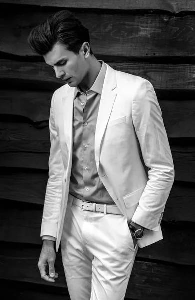 लकड़ी की दीवार के खिलाफ सफेद सूट में युवा सुंदर फैशनेबल आदमी का काला सफेद चित्र — स्टॉक फ़ोटो, इमेज