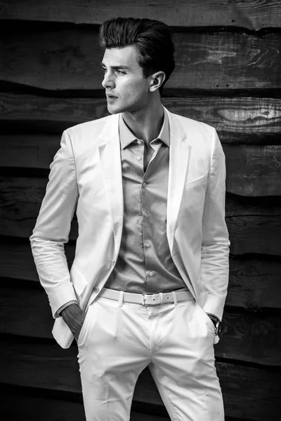 Retrato blanco y negro del joven guapo hombre de moda en traje blanco contra pared de madera —  Fotos de Stock