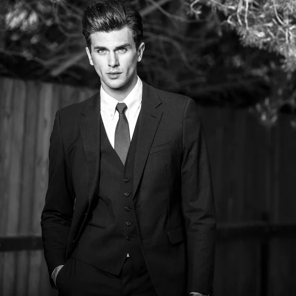 Retrato al aire libre blanco y negro de un hombre guapo elegante en traje clásico cerca de una cerca de madera — Foto de Stock