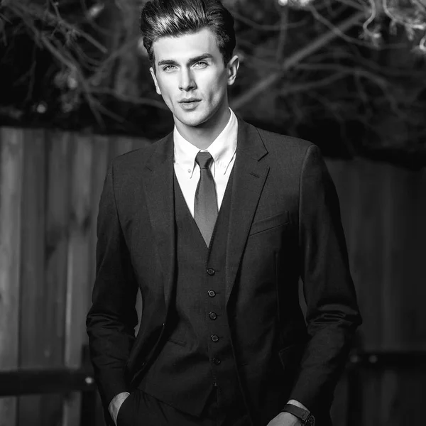 Schwarz-weißes Außenporträt eines eleganten gutaussehenden Mannes im klassischen Anzug in der Nähe von Holzzaun — Stockfoto