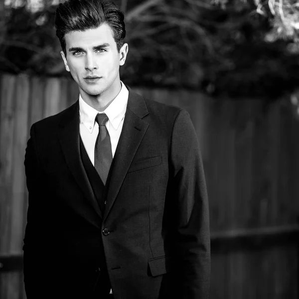 Retrato ao ar livre preto-branco de homem bonito elegante em terno clássico perto de cerca de madeira — Fotografia de Stock