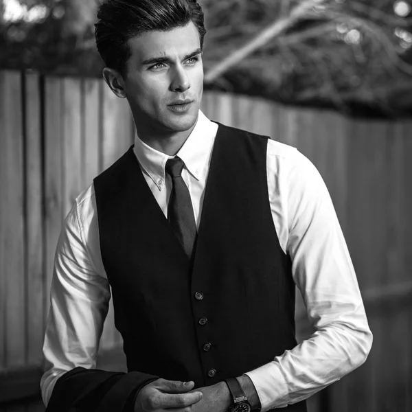 Portrait extérieur noir-blanc d'un élégant bel homme en gilet classique près d'une clôture en bois . — Photo
