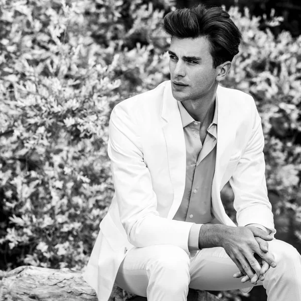 Retrato blanco y negro del joven guapo hombre de moda en traje blanco contra el fondo de la naturaleza —  Fotos de Stock