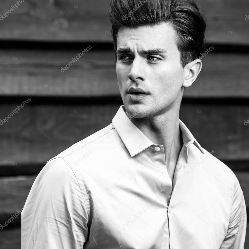 Black-white portrait of young handsome fashionable man against wooden wall.