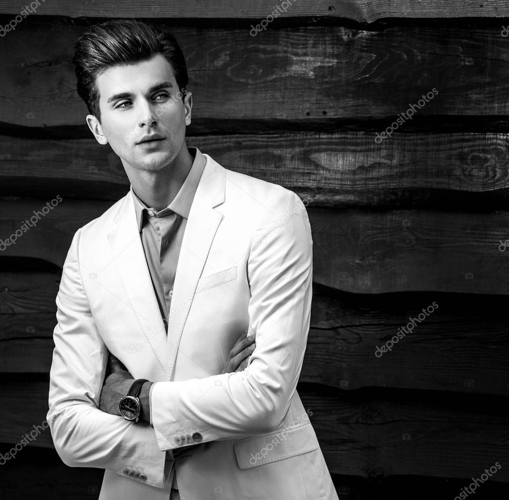 Black-white portrait of young handsome fashionable man in white suit against wooden wall