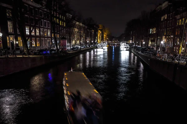 AMSTERDÃO, PAÍSES BAIXOS - JANEIRO 11, 2017: Belos canais noturnos da cidade de Amsterdã com barco de passageiros em movimento. 11 de janeiro de 2017 em Amsterdam - Países Baixos . — Fotografia de Stock