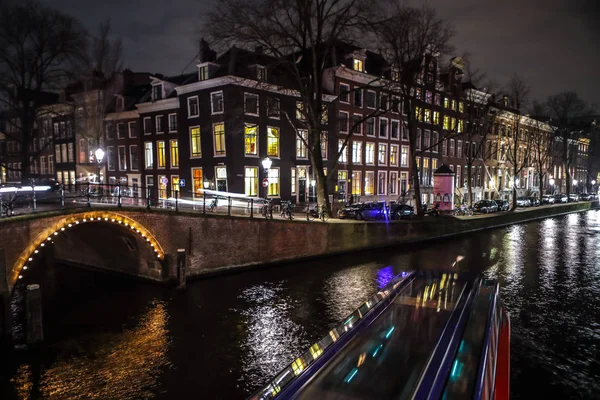 AMSTERDAM, PAÍSES BAJOS - 11 DE ENERO DE 2017: Hermosos canales nocturnos de la ciudad de Ámsterdam con barco pasajero en movimiento. 11 de enero de 2017 en Amsterdam - Países Bajos . — Foto de Stock