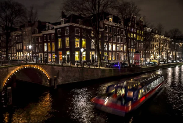 AMSTERDAM, PAÍSES BAJOS - 11 DE ENERO DE 2017: Hermosos canales nocturnos de la ciudad de Ámsterdam con barco pasajero en movimiento. 11 de enero de 2017 en Amsterdam - Países Bajos . —  Fotos de Stock