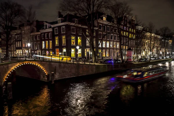 AMSTERDAM, PAÍSES BAJOS - 11 DE ENERO DE 2017: Hermosos canales nocturnos de la ciudad de Ámsterdam con barco pasajero en movimiento. 11 de enero de 2017 en Amsterdam - Países Bajos . — Foto de Stock