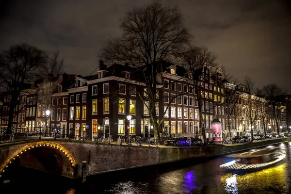 AMSTERDAM, PAÍSES BAJOS - 11 DE ENERO DE 2017: Hermosos canales nocturnos de la ciudad de Ámsterdam con barco pasajero en movimiento. 11 de enero de 2017 en Amsterdam - Países Bajos . — Foto de Stock