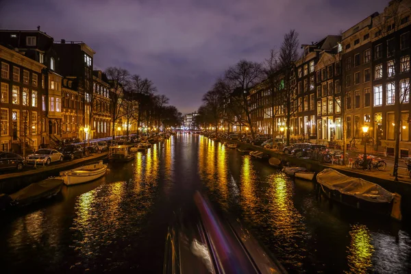 AMSTERDAM, PAÍSES BAJOS - 12 DE ENERO DE 2017: Hermosos canales nocturnos de la ciudad de Ámsterdam con barco pasajero en movimiento. 12 de enero de 2017 en Amsterdam - Países Bajos . — Foto de Stock