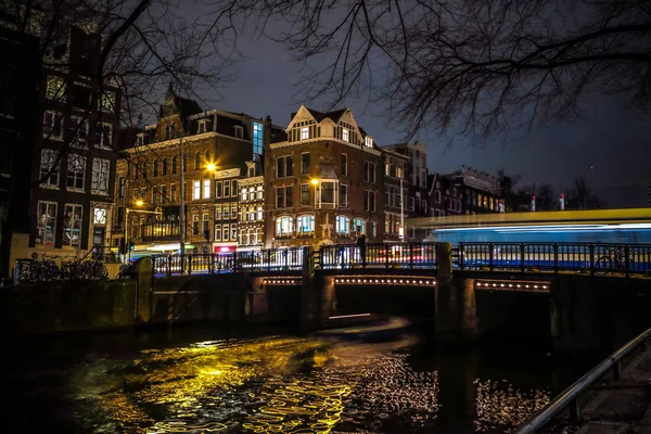 AMSTERDAM, PAÍSES BAJOS - 08 DE ENERO DE 2017: Los tranvías pasan por el viejo puente en la ciudad de Ámsterdam por la noche. enero 08, 2017 en Amsterdam - Países Bajos . — Foto de Stock