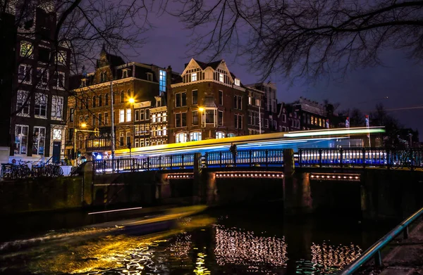 AMSTERDAM, PAÍSES BAJOS - 08 DE ENERO DE 2017: Los tranvías pasan por el viejo puente en la ciudad de Ámsterdam por la noche. enero 08, 2017 en Amsterdam - Países Bajos . — Foto de Stock