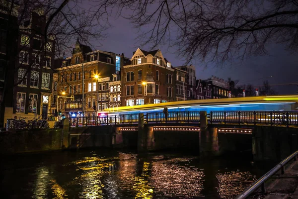 АМСТЕРДАМ, НИДЕРЛАНДЫ - 08 ЯНВАРЯ 2017: Трамваи ездят по старому мосту в Амстердаме ночью. Январь 08, 2017 в Амстердаме - Нидерланды . — стоковое фото