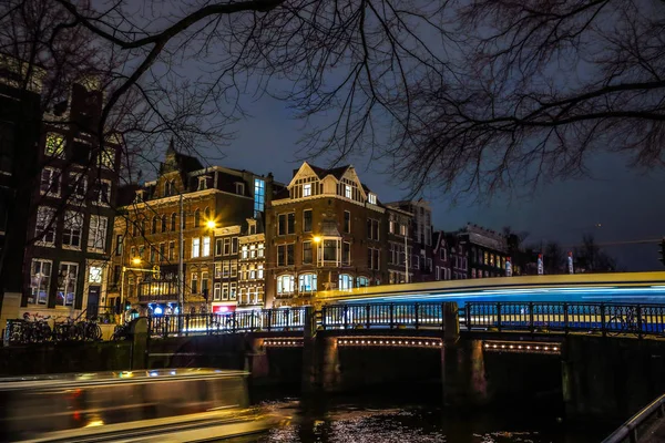 AMSTERDÃO, PAÍSES BAIXOS - JANEIRO 08, 2017: Os bondes passam pela velha ponte na cidade de Amsterdã à noite. 08 de janeiro de 2017 em Amsterdam - Países Baixos . — Fotografia de Stock