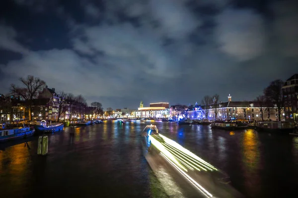 AMSTERDÃO, PAÍSES BAIXOS - JANEIRO 12, 2017: Belos canais noturnos da cidade de Amsterdã com barco de passageiros em movimento. 12 de janeiro de 2017 em Amsterdam - Países Baixos . — Fotografia de Stock