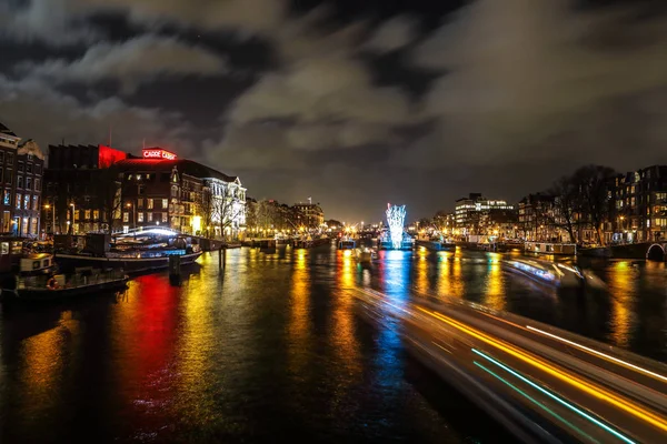 AMSTERDAM, NETHERLANDS - JANUARY 12, 2017: Beautiful night city canals of Amsterdam with moving passanger boat. January 12, 2017 in Amsterdam - Netherland. — Stock Photo, Image