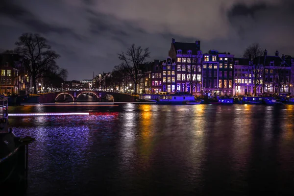 AMSTERDAM, PAÍSES BAJOS - 12 DE ENERO DE 2017: Hermosos canales nocturnos de la ciudad de Ámsterdam con barco pasajero en movimiento. 12 de enero de 2017 en Amsterdam - Países Bajos . — Foto de Stock