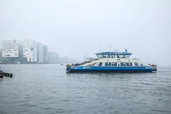 Amsterdam, Nederländerna - 02 januari 2017: Båtar på staden kanal nära piren i Central station i dimmig dag. 02 januari 2017 i Amsterdam - Nederländerna. — Stockfoto