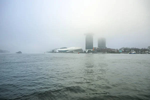 Överblick över staden kanal nära piren i Amsterdam Central station i dimmig dag. — Stockfoto