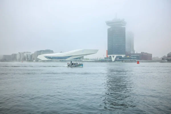 Amsterdam, Nederländerna - 02 januari 2017: Båtar på staden kanal nära piren i Central station i dimmig dag. 02 januari 2017 i Amsterdam - Nederländerna. — Stockfoto