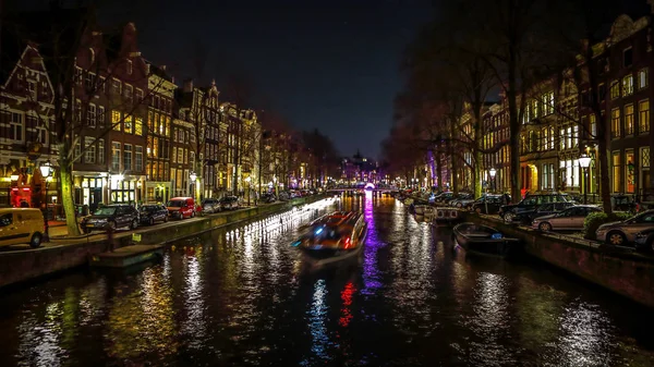 AMSTERDAM, PAÍSES BAJOS - 11 DE ENERO DE 2017: Hermosos canales nocturnos de la ciudad de Ámsterdam con barco pasajero en movimiento. 11 de enero de 2017 en Amsterdam - Países Bajos . — Foto de Stock