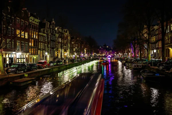 AMSTERDAM, PAÍSES BAJOS - 11 DE ENERO DE 2017: Hermosos canales nocturnos de la ciudad de Ámsterdam con barco pasajero en movimiento. 11 de enero de 2017 en Amsterdam - Países Bajos . —  Fotos de Stock