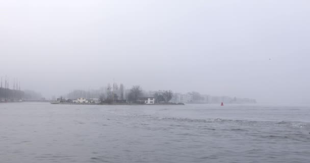 霧の日の中央駅の桟橋付近都市チャネルのアムステルダム, オランダ - 2017 年 1 月 2 日: ボート。4 k ビデオ。2017 年 1 月 2 日アムステルダム - オランダ. — ストック動画