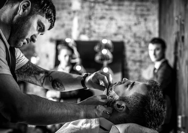 Master makes beards correction in barbershop salon. Black-white photo. — Stock Photo, Image