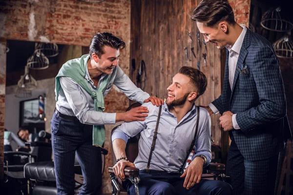 Tre unga eleganta positiva vänner pose i inre av barbershop. — Stockfoto