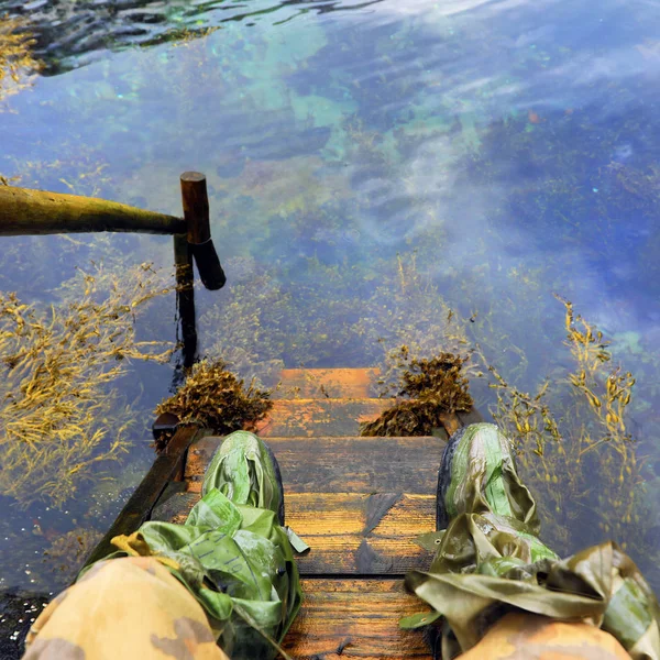 在清澈的水河和橡胶旅游鞋的老木步骤涵盖特写. — 图库照片