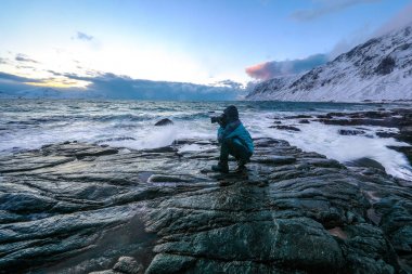 Seyahat fotoğrafçı akşam anda soğuk Norveç Denizi kıyısında antik taşlar resimleri yapıyor. Lofoten Adaları. Güzel Norveç manzara. 