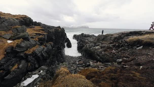 Fotógrafo de viajes haciendo fotos en piedras antiguas a orillas del frío mar de Noruega a la hora de la tarde. Islas Lofoten. Hermoso paisaje de Noruega. HD de imágenes . — Vídeos de Stock